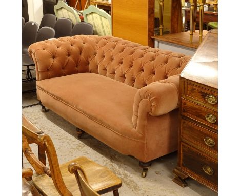 A Victorian button-back upholstered rollover arm Chesterfield settee, raised on 6 mahogany turned legs with brass casters, L2