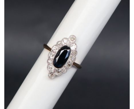 A sapphire and diamond ring, set with an elongated oval sapphire surrounded by round old cut diamonds to a white metal settin