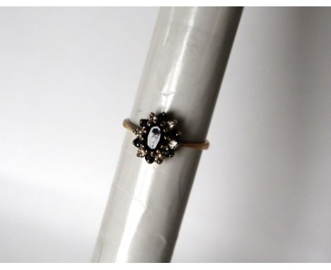 A sapphire and diamond cluster ring, set with a raised central oval faceted sapphire surrounded by alternating sapphires and 