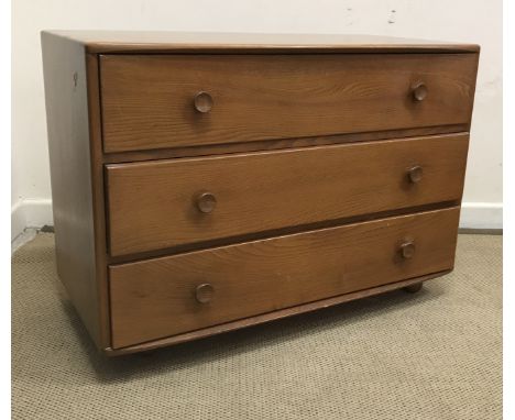 An Ercol elm chest, the shallow bow fronted top over three drawers with turned knob handles on castors, 91.5 cm wide x 48 cm 