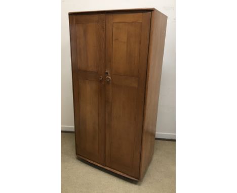 An Ercol elm wardrobe, the shallow bow fronted top over two cupboard doors enclosing a hanging space on castors, 91 cm wide x