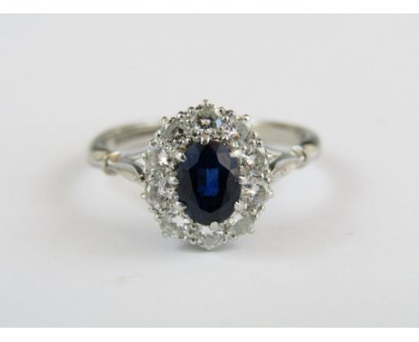 A diamond and sapphire flowerhead cluster dress ring, the central oval stone of approximately 0.6ct, claw set above a frame o