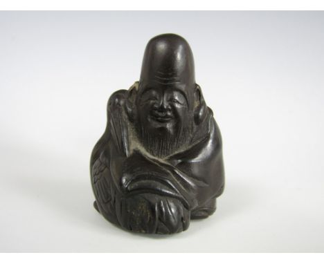 A Meiji Japanese black-glazed earthenware netsuke modelled as a sage or immortal sat with a pelican
