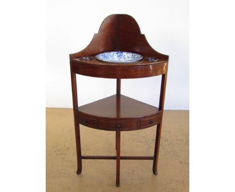 A George III mahogany bow-fronted corner wash stand, having a gallery back above a shelf fitted for and containing a blue-and