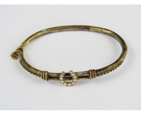 A Victorian yellow-metal and seed pearl hinged bangle, having a pair of parallel bars to the centre, surmounted by a pearl se