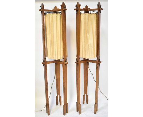 A pair of oak Arts and Crafts style standard lamps, each with three carved supports and cream drapes on rails, height 193cm (