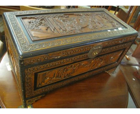 Oriental heavily carved camphor wood trunk with figural panels and hinged top with brass lock plate. (B.P. 24% incl. VAT)