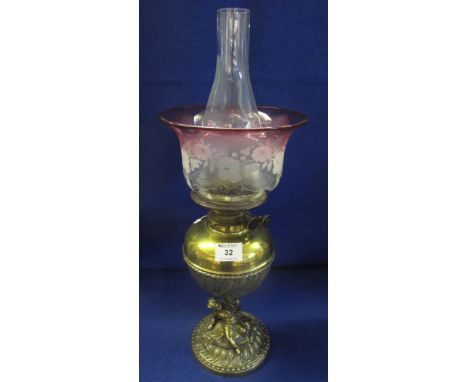 Early 20th Century brass double burner oil lamp with brass reservoir and figural brass base, having cranberry shade and folia