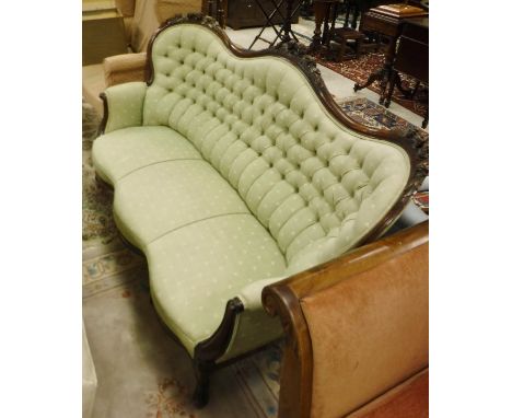 A Victorian three seat sofa in pale green button back upholstery, the stained frame topped by floral carvings to the serpenti