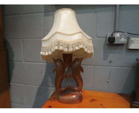 A carved hardwood figural table lamp in the form of dolphins with pleated shade 
