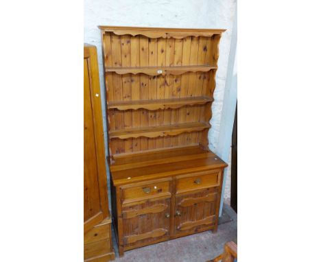 A 1.16m modern stained pine two part dresser with decorative three shelf open plate rack over a base with two frieze drawers 