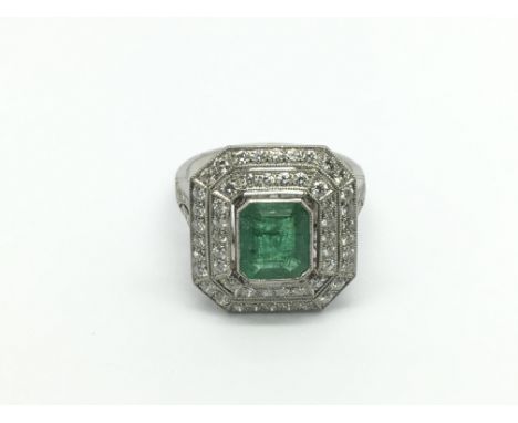 A platinum ring set with a large emerald cut central emerald and surrounded by two octagonal halos of diamonds with further d