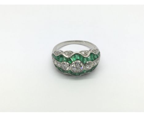 A platinum, emerald and diamond dress ring set with three graduated old cut diamonds, calibre cut emeralds and diamonds, diam