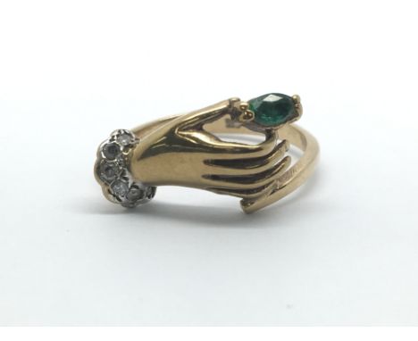 A 9ct yellow gold ring in the style of a hand holding an emerald with diamond cuff, ring size approx L