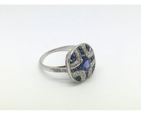 A Victorian style platinum sapphire and diamond panel ring set with a central oval cut sapphire, RBC diamonds and calibre cut