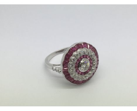 A platinum, ruby and diamond dress ring set with a central old cut diamond, a halo of rubies, a halo of diamonds and an outer