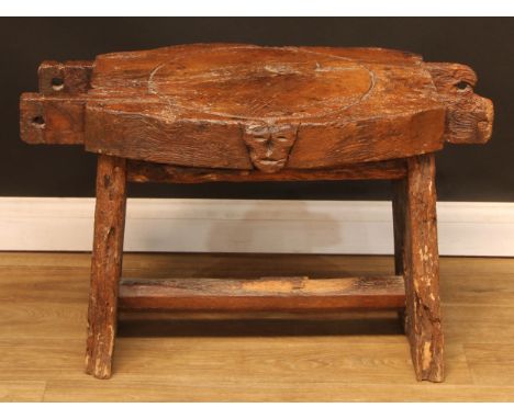 A 19th century elm cheese or fruit press bed, carved with a primitive skull, 83cm wide, 44cm deep, later mounted as a table, 