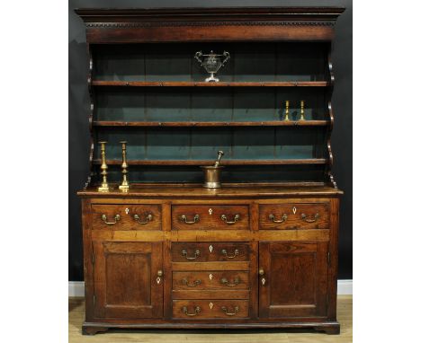 A George III oak and elm dresser, moulded cornice with dentil capital above three plate rack shelves, the projecting base wit