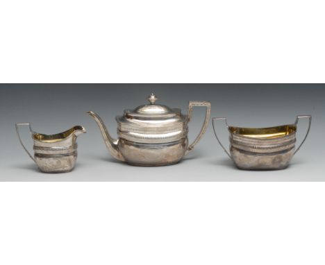 A George III silver three piece boat shaped tea service, comprising teapot, milk jug and sugar basin, bright-cut engraved and