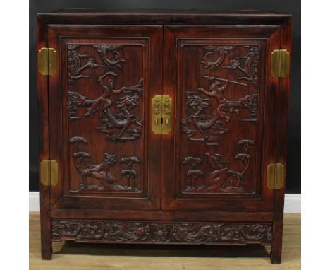 A Chinese hardwood side cabinet, flush rectangular top above a pair of panel doors carved with duelling warriors on dragonbac
