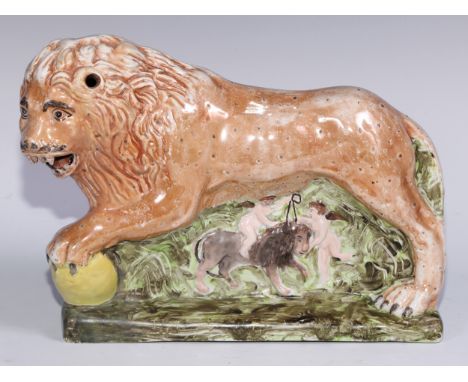 A large pearlware model of a lion, he stands, roaring, his paw upon a sphere, the base moulded with putti, lustre glaze, 32cm