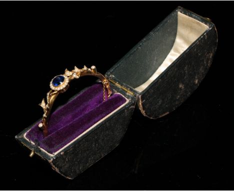 A late 19th/early 20th century 15ct gold hinged bangle bracelet, set with a central sapphire accented with seed pearls as a f