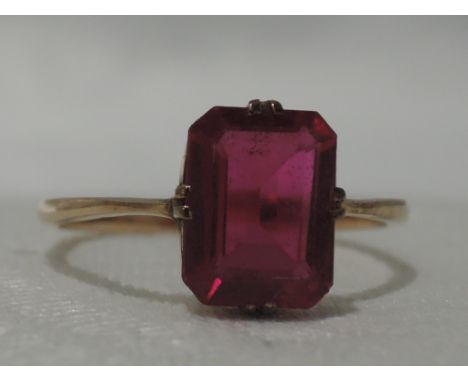 A lady's dress ring having an emerald cut synthetic ruby in a claw set mount on a yellow metal loop stamped 9ct, size N