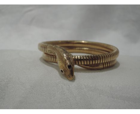 A 9ct gold snake bangle having ruby eyes and engraved decoration to head, coiled body with steel spring, Chester hallmarks, m