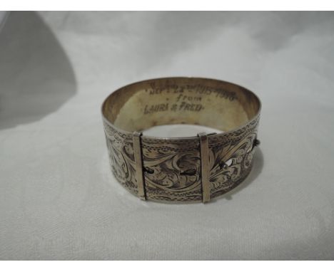 A white metal bangle stamped sterling silver modelled as a belt having engraved decoration, bearing inscriptions to inside