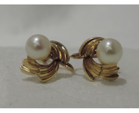 A pair of yellow metal screw back Mikimoto pearl earrings stamped 14K having gold swirl surrounds