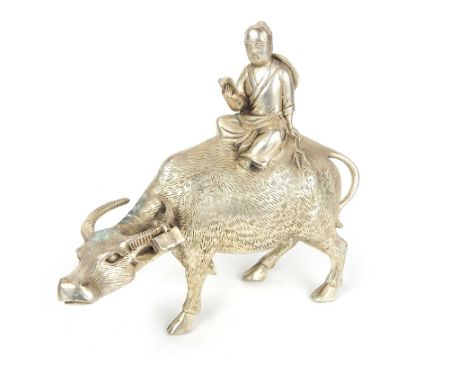 A Chinese white metal model of a standing oxen with a model of a Chinese man reading a book sat on the oxen's back, 25 x 27.5