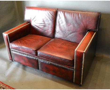 A Burgundy Leather And Brass Studded Three Piece Suite comprising a three seater sofa, a matching two seater sofa and an armc