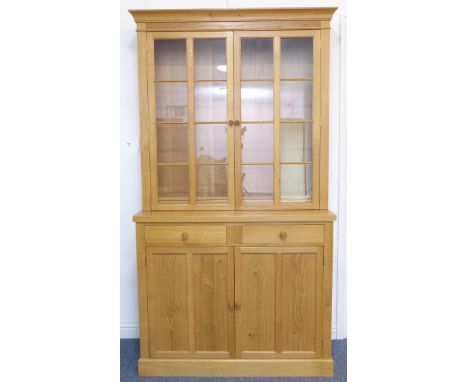 A modern light oak display cabinet; cavetto style cornice above two glazed doors with moulded astragal glazing bars enclosing