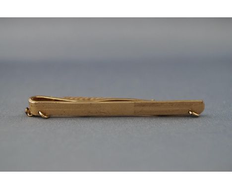 A yellow metal tie slide with engine turned finish. Having attached safety chain. Stamped 9ct back and front., MG&amp;S. 6.6 