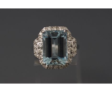 A white metal aquamarine and diamond cluster ring set with an emerald cut aquamarine of approximately 6.89cts and round brill