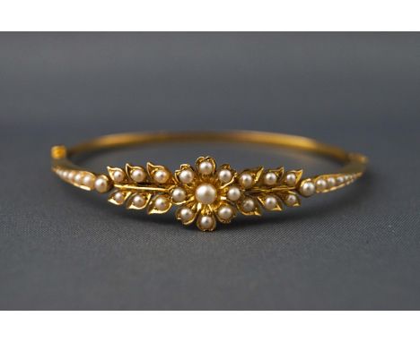 A yellow metal hinged bangle set with seed pearls in a floral and leaf design. Push in clasp with additional loops for safety