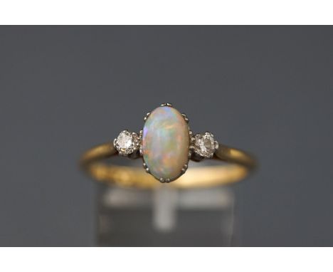 A yellow and white metal three stone ring set with an oval cabochon cut opal flanked by one round brilliant cut diamond to ea