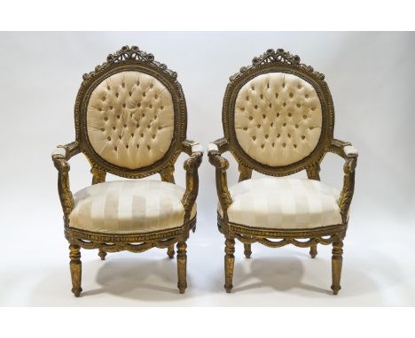 A pair of French elbow chairs each with carved frames and button backs, later painted in gold
