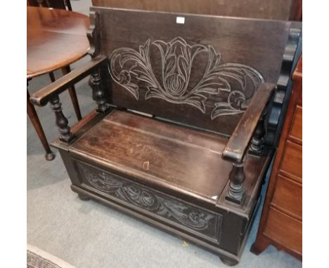 An early 20th century carved oak monks' bench, the pivoting back support above a hinged seat with turned spindle armrests abo