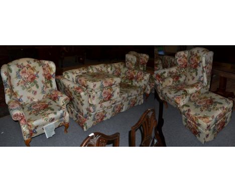 A pair of floral upholstered wing back arm chairs; together with a three-seater sofa and pair of footstools in matching uphol