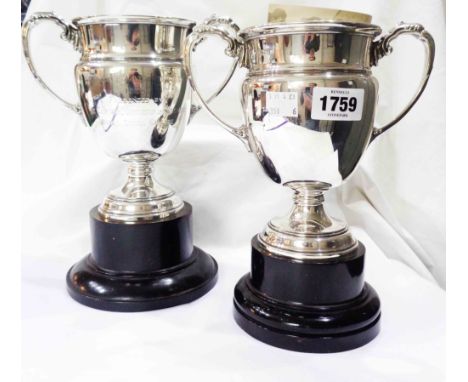 A pair of 16.5cm silver trophy cups with flanking cast acanthus scroll handles, set on matching ebonised socle bases - both w