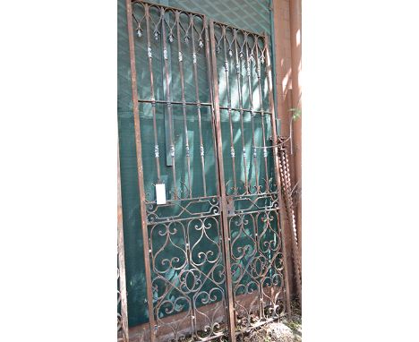 A PAIR OF WROUGHT IRON GATES each with scroll and linear panels, remnants of paint, each gate 237 x 59cm