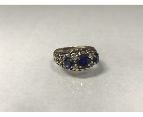 BLUE AND WHITE GEM SET RING the three graduated oval blue stones interspaced by round white gems, within an openwork bezel, i