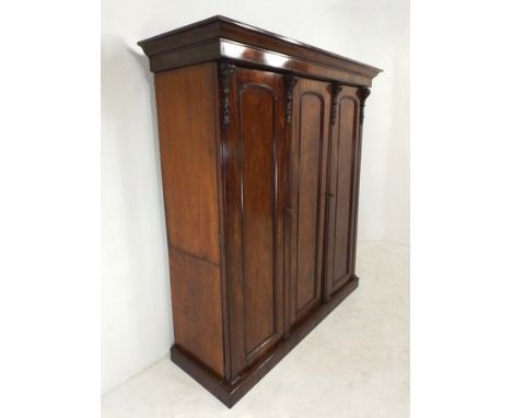 A Victorian mahogany three door compactum wardrobe, the outswept cornice and plain frieze supported on four foliate and scrol