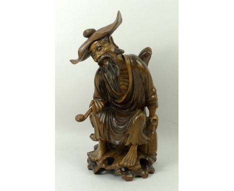 A Chinese hardwood carving of an aged man, 20th century, modelled seated with a hat, pipe and a basket, 22cm high.