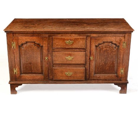 A Georgian oak dresser, the rectangular plank top above three central drawers with brass handles, flanked by two fielded pane