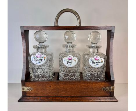 An early 20th Century oak tantalus, with three glass decanters and porcelain spirit labels 