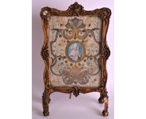 A RARE 17TH/18TH CENTURY EUROPEAN SILKWORK TABLE SCREEN with carved giltwood mounts, set centrally with a portrait of a saint