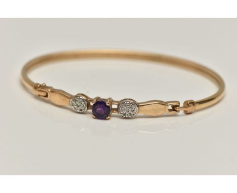 A 9CT GOLD GEM SET BANGLE, set with a central circular cut amethyst, flanked with single cut diamond accents, hook fitting on