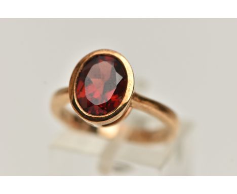 A 9CT GOLD GARNET RING, oval cut garnet in a collet setting, mount measuring approximately length 11.5mm x width 9.8mm, pinch